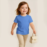 Child wearing a blue shirt and beige pants holding a small handbag against a plain background