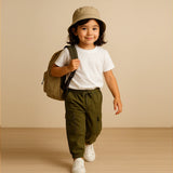 Child wearing a beige hat, white shirt, green pants, and carrying a green backpack on a beige background